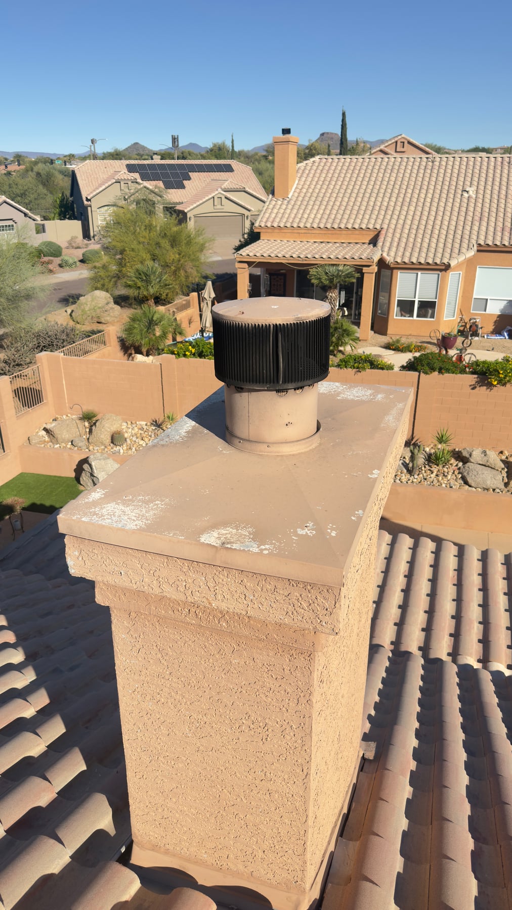 Black metal chimney cap on stucco chimney with terracotta tile roof in Arizona