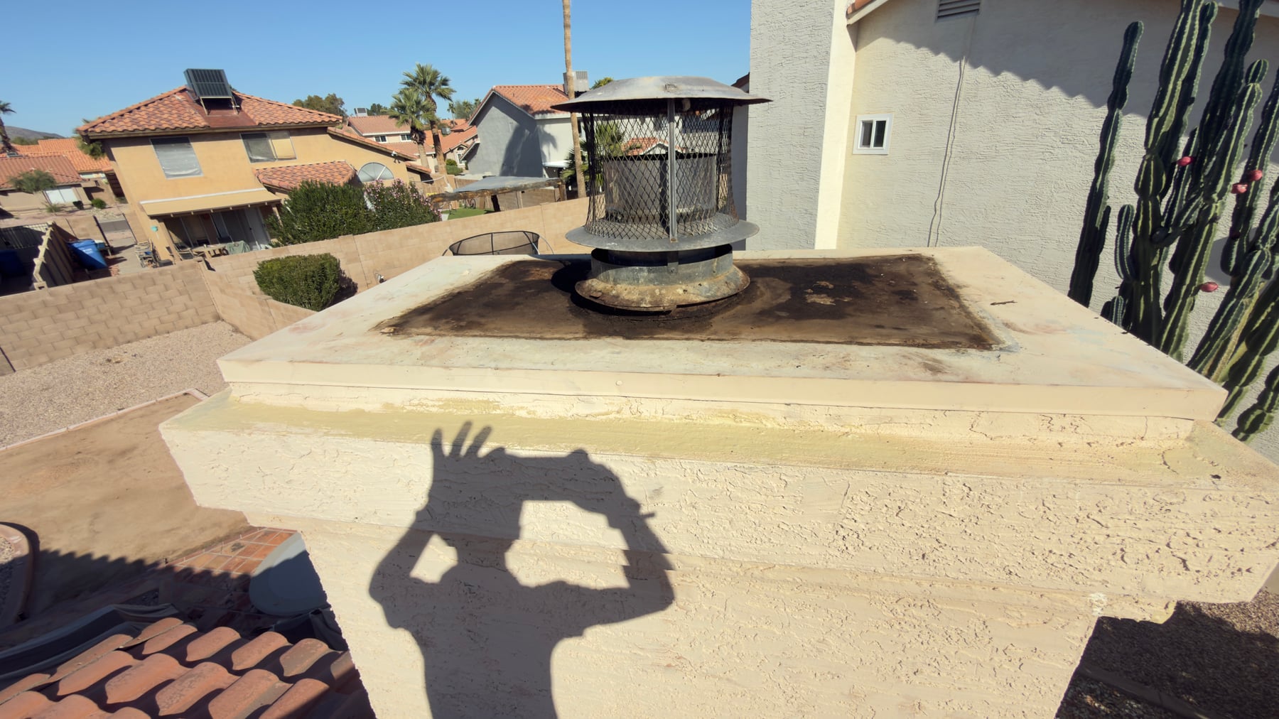 Black metal chimney cap on stucco chimney with terracotta tile roof in Arizona