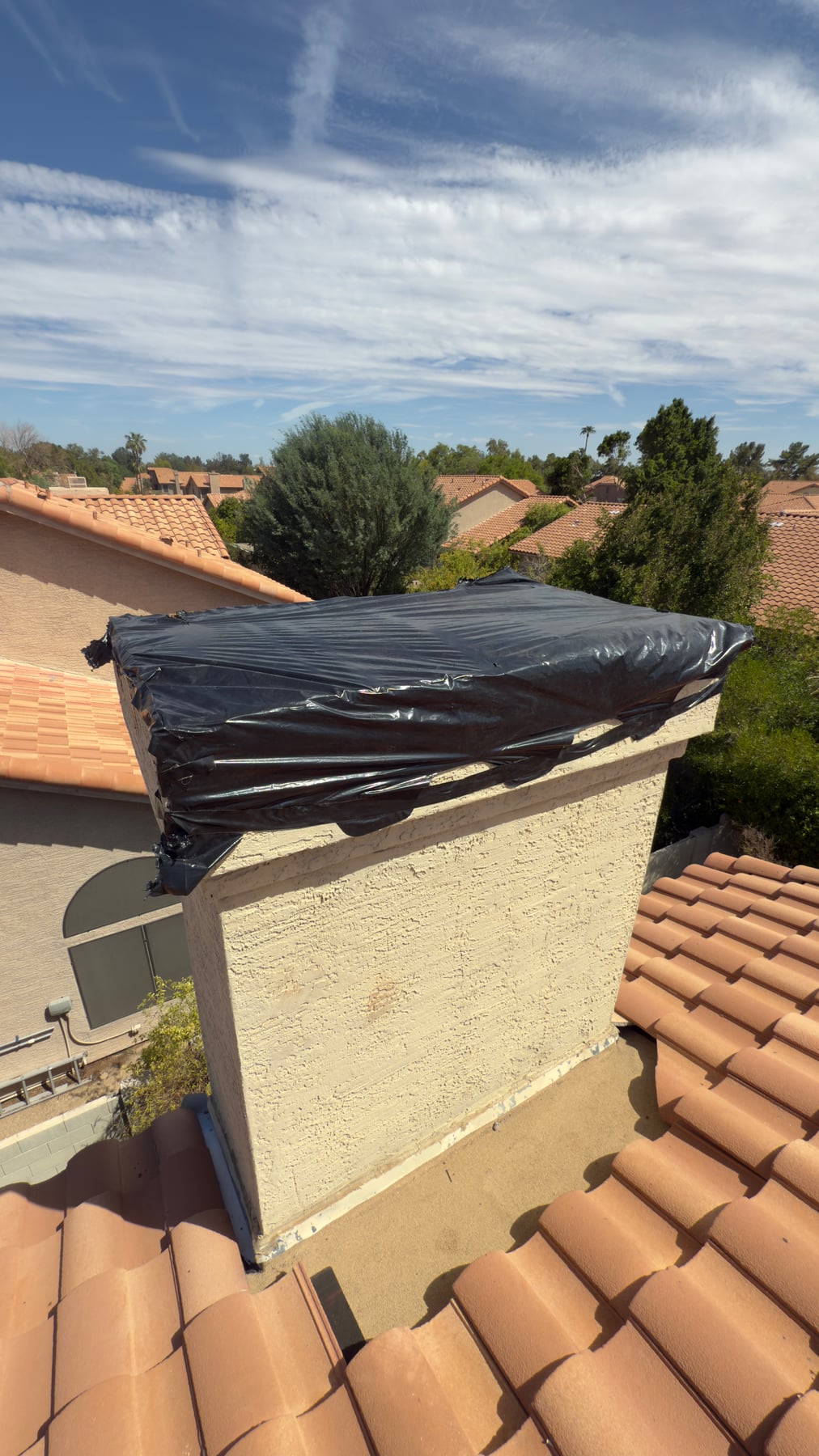 Chimney top covered with black plastic sheeting as temporary leak protection in Arizona