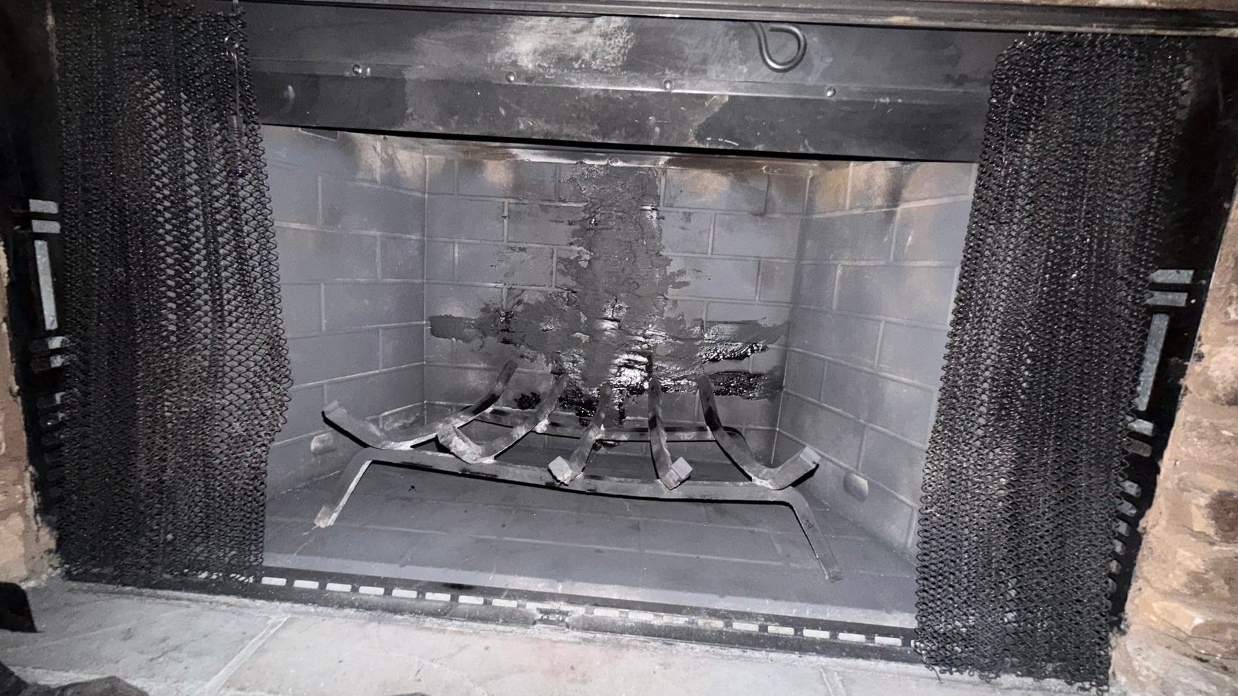 Fireplace firebox with heavy creosote buildup on refractory brick walls and log grate
