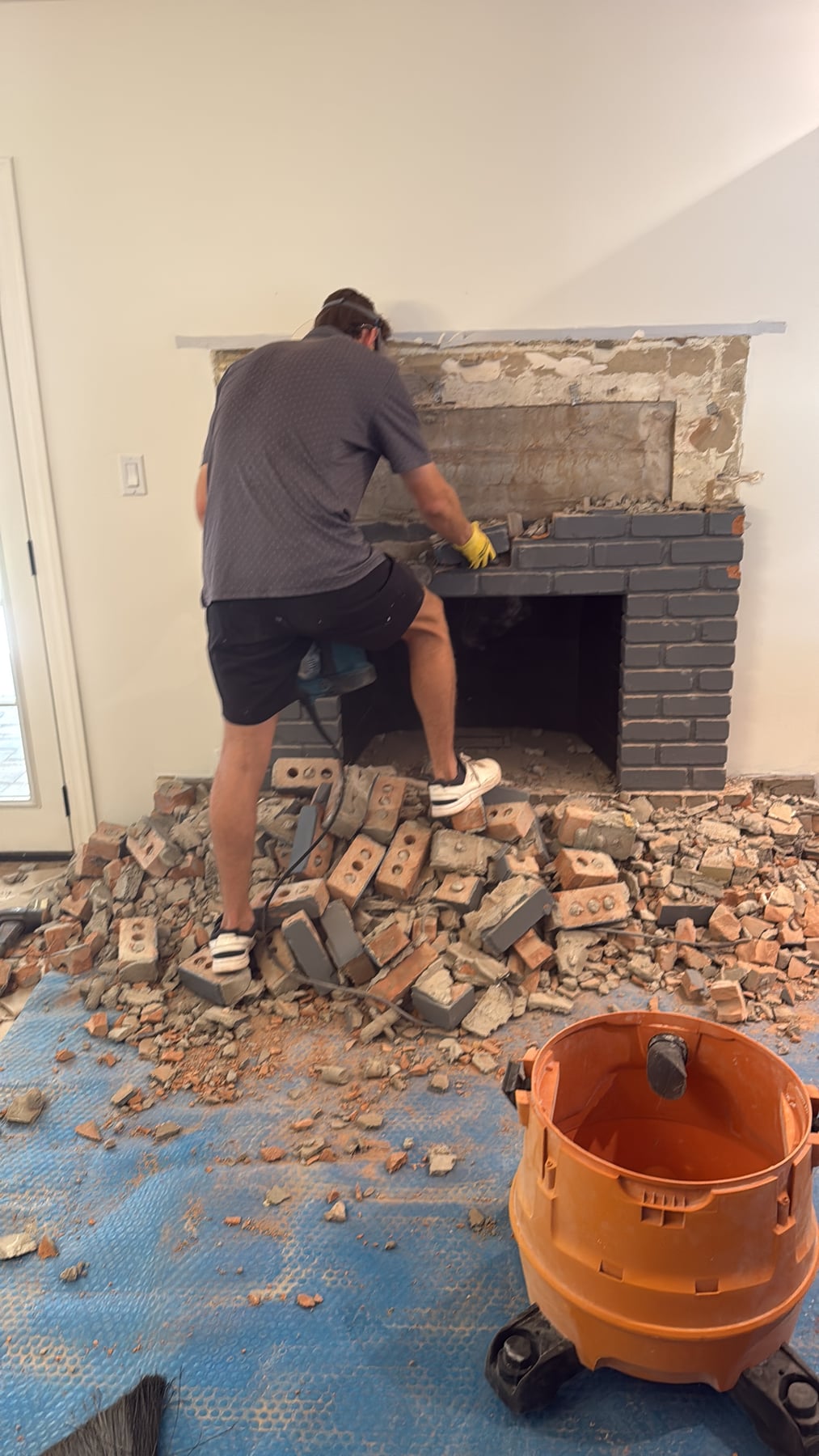 Technician demolishing brick fireplace surround during remodel with debris on floor